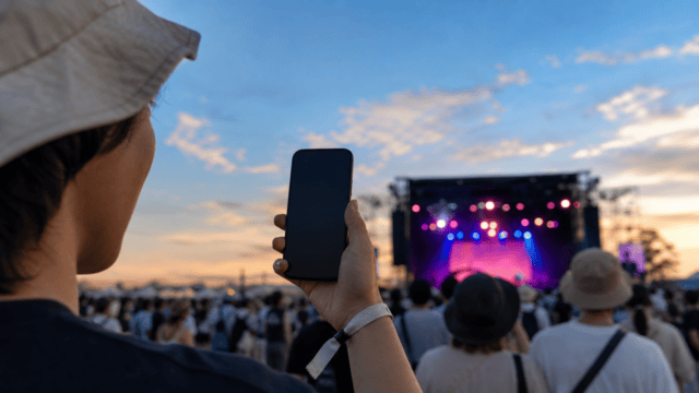 野外音楽フェス会場でスマートフォンを確認する来場者のイメージ